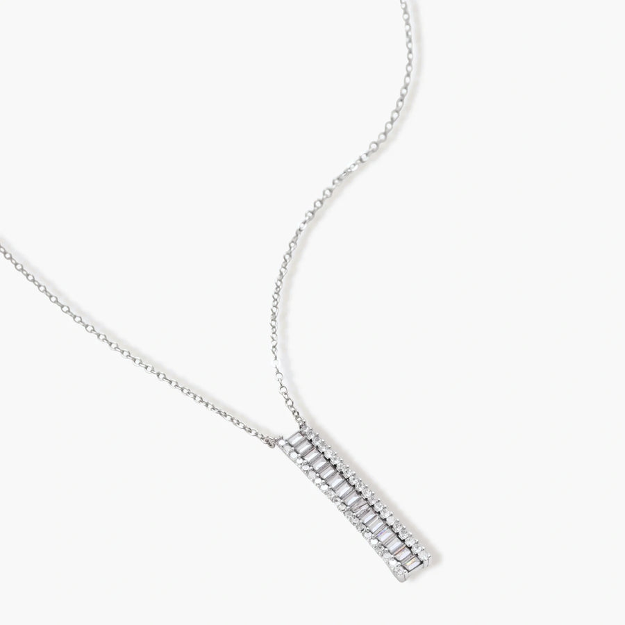 White gold plated necklace with vertical cubic zirconia pendant and matching hoop earrings on neutral background