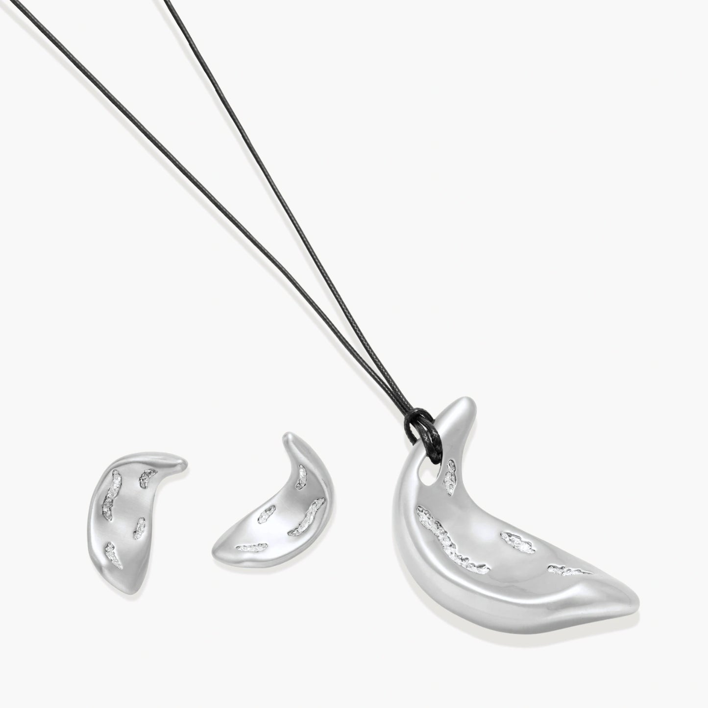 Crescent moon shaped pendant and earrings in eco-zinc alloy with curved crystal inlay patterns on light background.