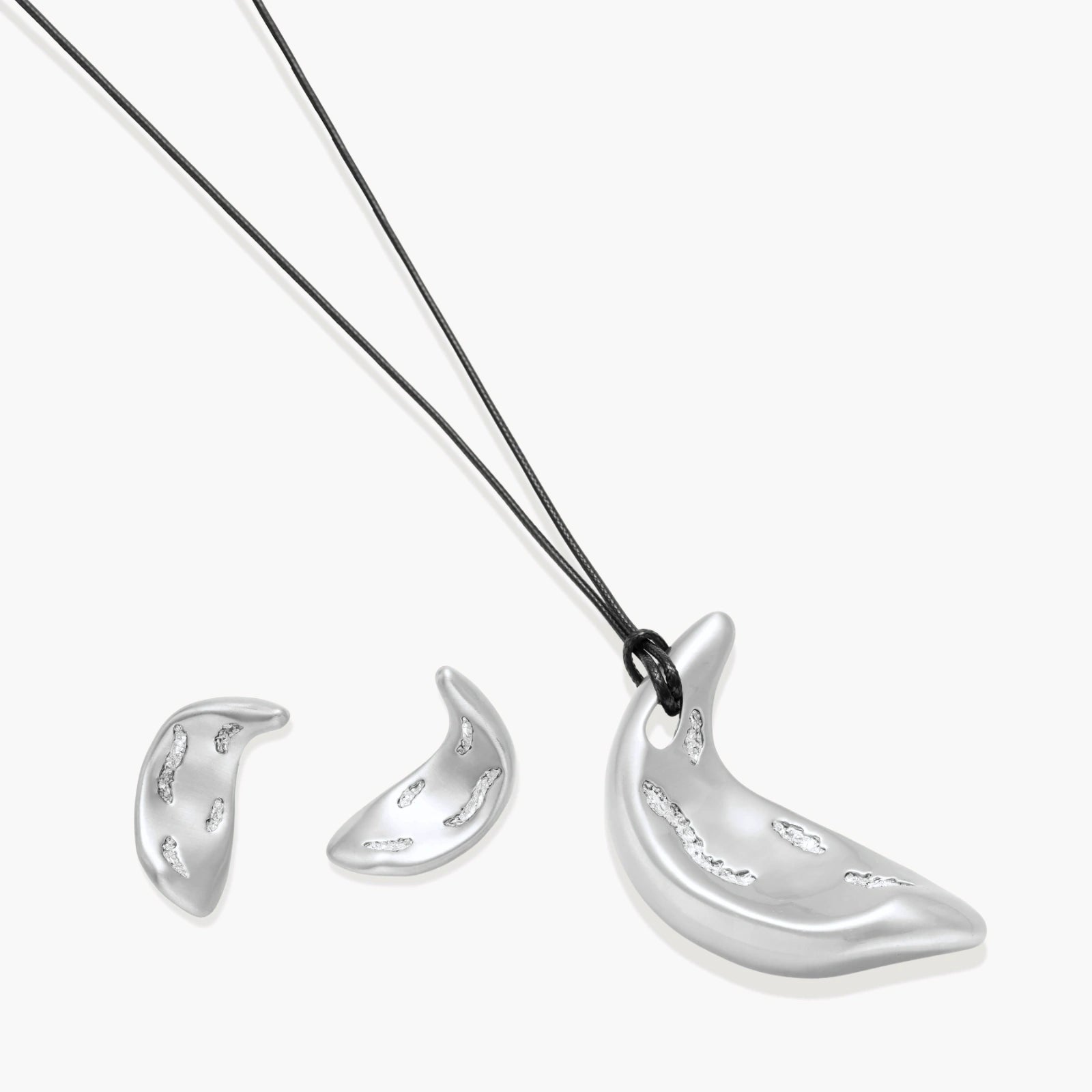 Crescent moon shaped pendant and earrings in eco-zinc alloy with curved crystal inlay patterns on light background.