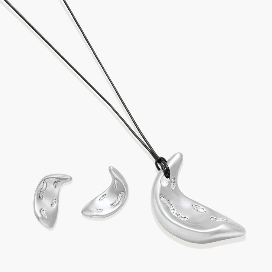 Crescent moon shaped pendant and earrings in eco-zinc alloy with curved crystal inlay patterns on light background.