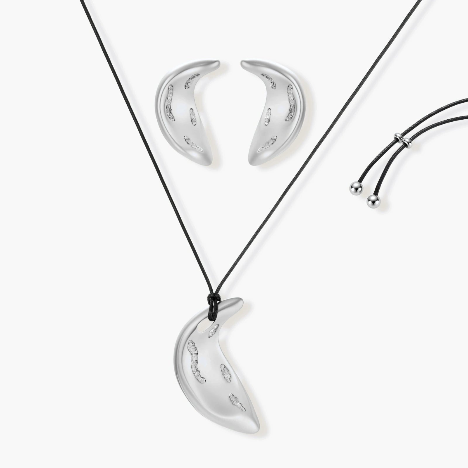 Crescent moon shaped pendant and earrings in eco-zinc alloy with curved crystal inlay patterns on light background.