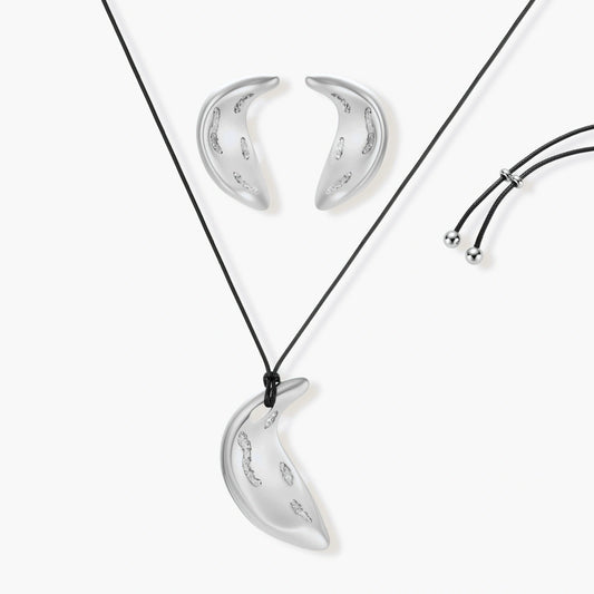 Crescent moon shaped pendant and earrings in eco-zinc alloy with curved crystal inlay patterns on light background.
