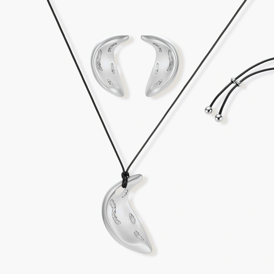 Crescent moon shaped pendant and earrings in eco-zinc alloy with curved crystal inlay patterns on light background.